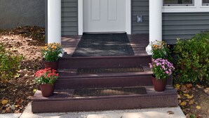 A house with a front porch, a white door, and two potted plants. - Kayaks - Firepit - Dock - Fishing & more! (Lindstrom)