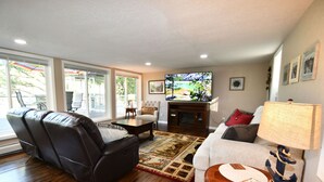 A living room with a leather sofa, a white armchair, a coffee table, and a television. - Kayaks - Firepit - Dock - Fishing & more! (Lindstrom)