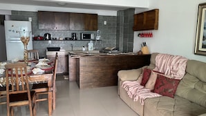 A modern kitchen with dark wooden cabinets, a central island, and a dining area with a table and chairs. - Desfrute dessa maravilha. (Angra dos Reis)