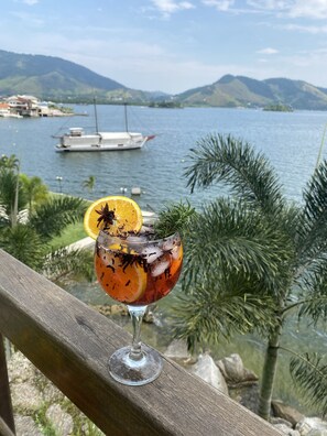 A cocktail on a wooden railing with a lake and mountains in the background. - Desfrute dessa maravilha. (Angra dos Reis)
