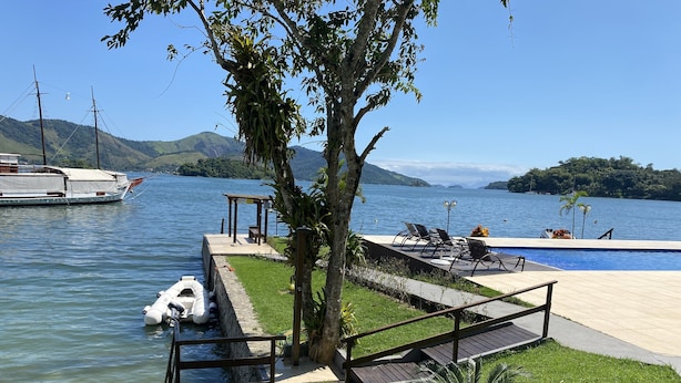 A lakeside pool area with a wooden deck, lounge chairs, and a small boat docked near the water. - Desfrute dessa maravilha. (Angra dos Reis)