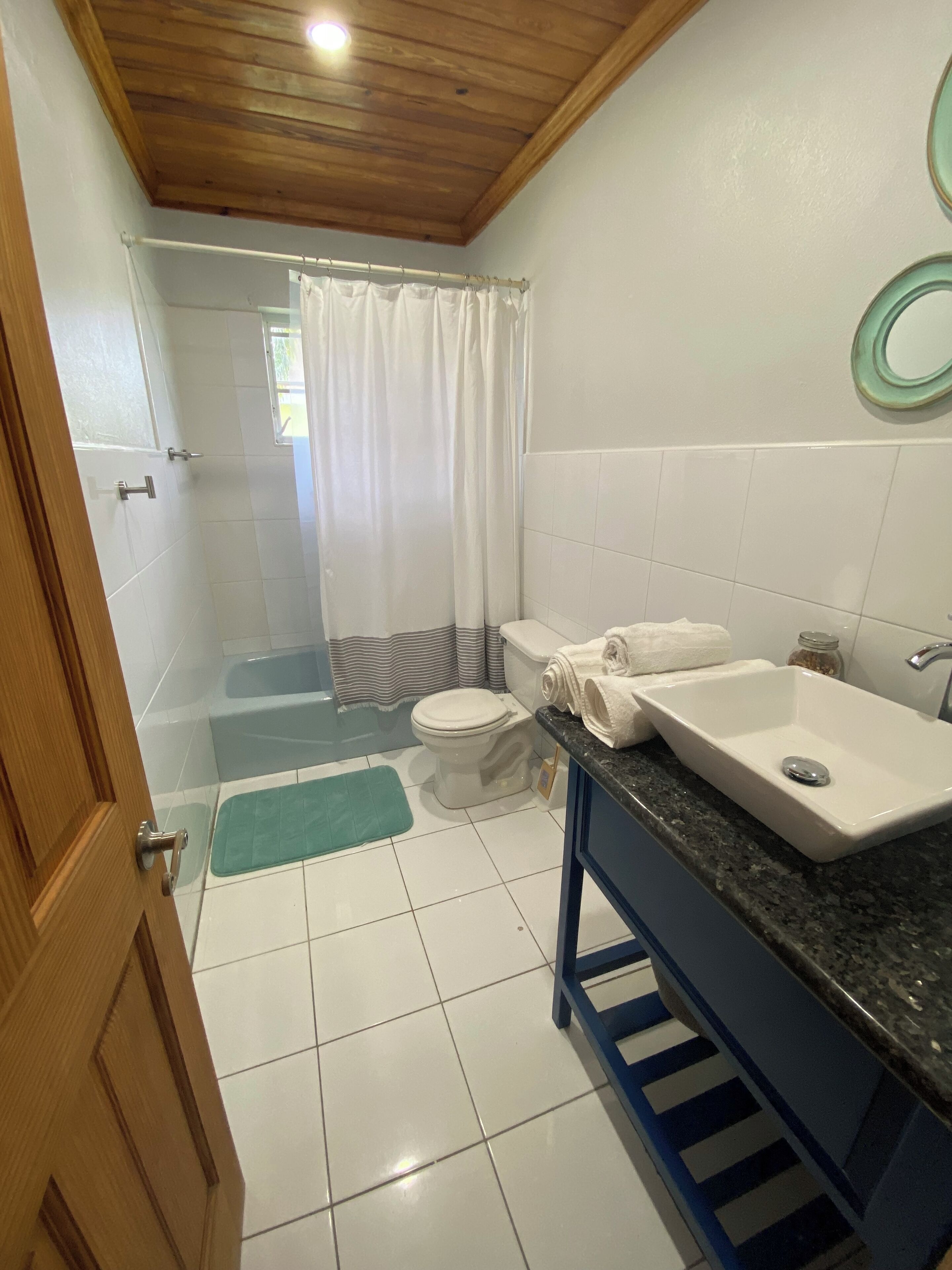 A bathroom with a wooden ceiling, white tiles, a bathtub, a toilet, and a sink.