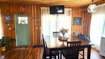 A wooden-paneled room with a dining table, chairs, a TV, and a door with an exit sign.