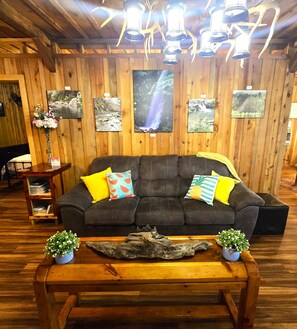 A cozy room with a wooden ceiling, a dark grey sofa with colorful cushions, and a wooden coffee table. - Unique Farmhouse Modern Country Cabin (Mena)