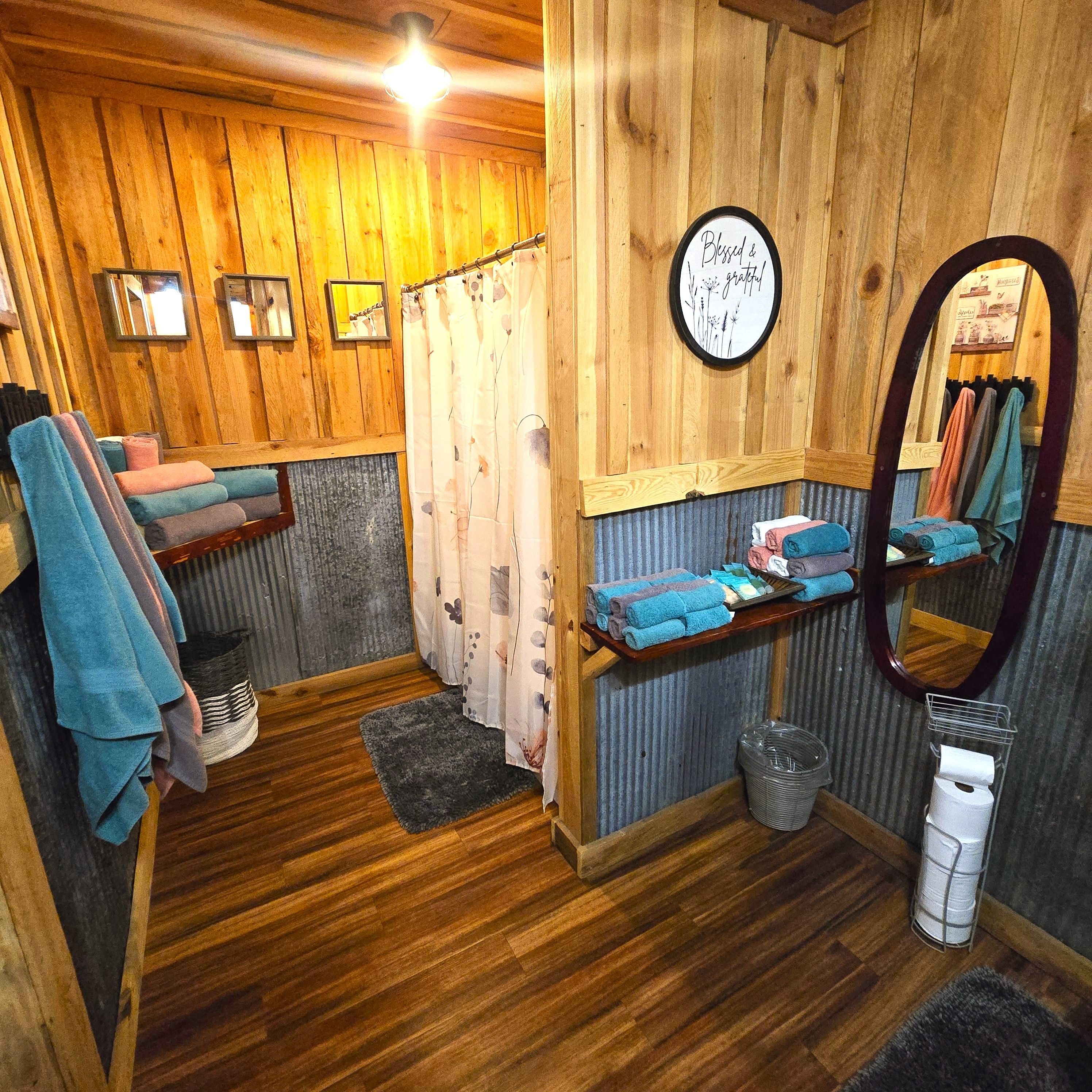 Interior de madera con ducha, toallas, un espejo y un letrero.