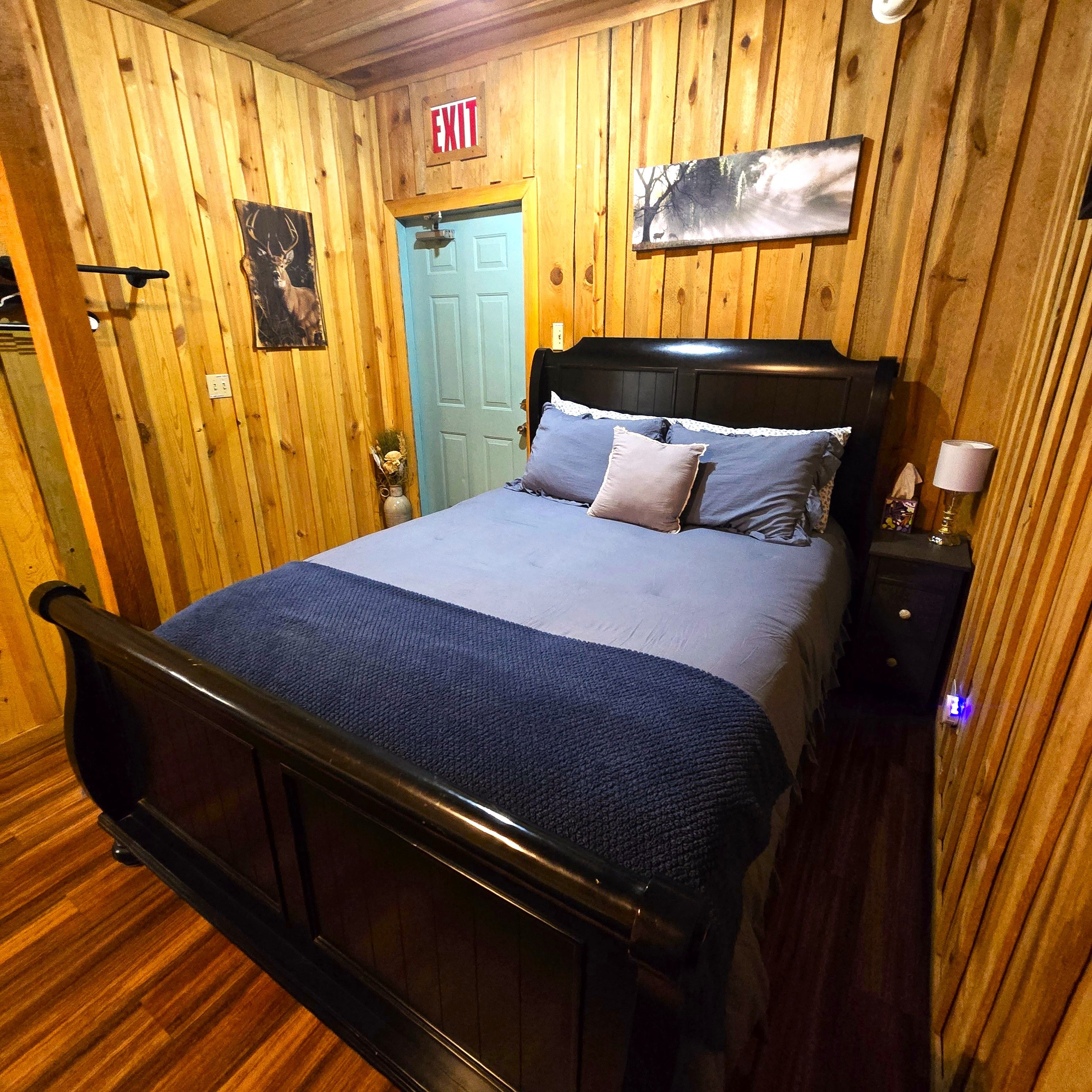 A wooden-paneled room with a bed, a door marked 'EXIT', and a wall-mounted picture.