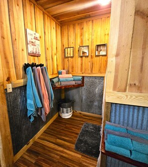 Een badkamer met houten wanden, een houten bankje, een handdoekhouder, een plank met handdoeken en een kleine prullenbak.