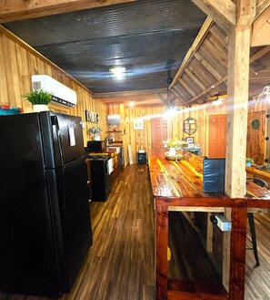 Cocina con paredes y suelo de madera, equipada con un refrigerador negro y una mesa de comedor de madera.