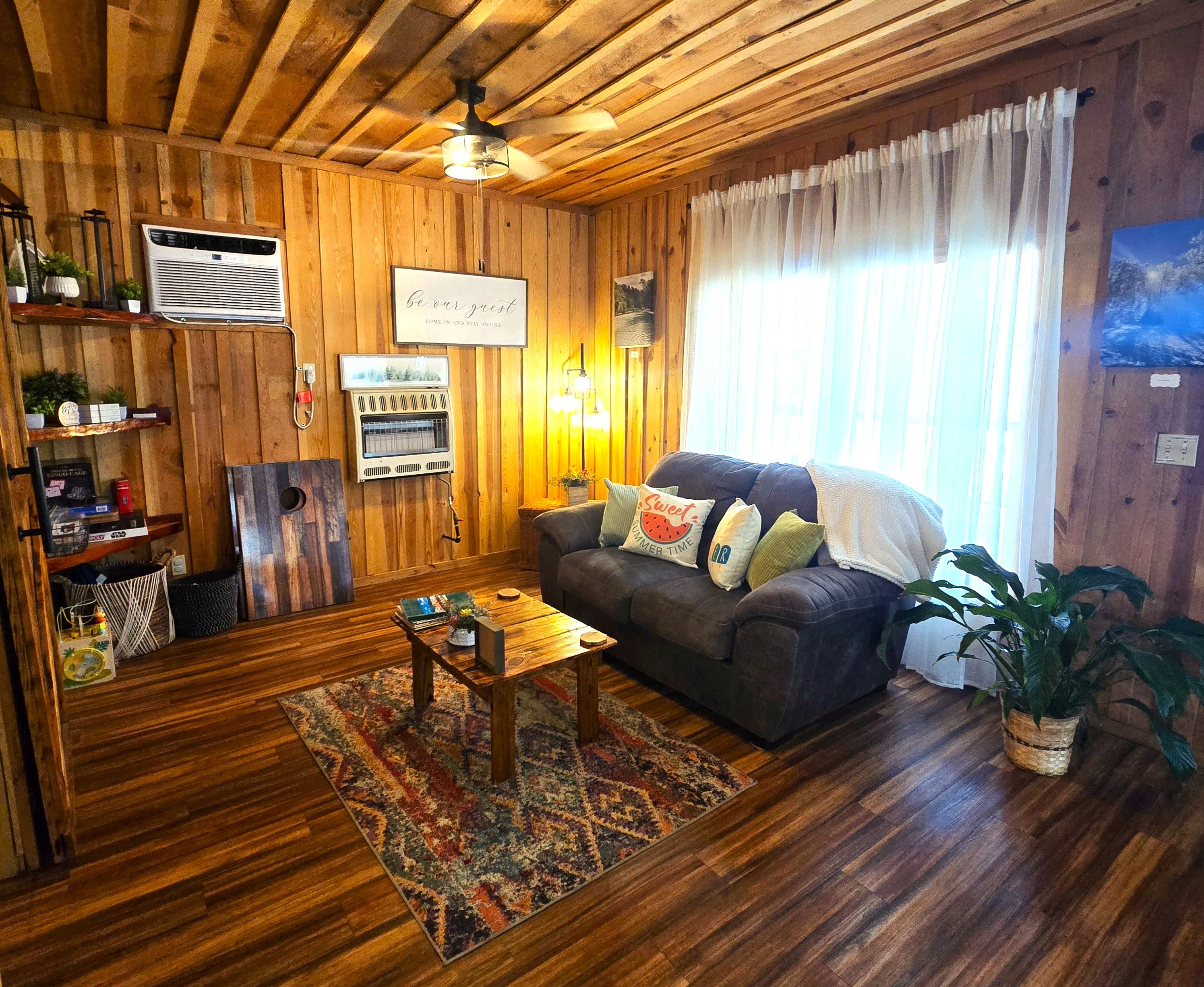 Una sala de estar acogedora con paredes de madera, un ventilador de techo, un sofá con cojines, una mesa de centro y una alfombra.