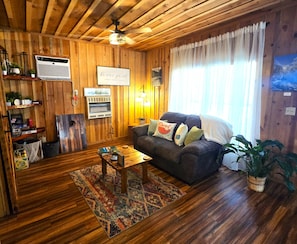 Una sala de estar acogedora con paredes de madera, un ventilador de techo, un sofá con cojines, una mesa de centro y una alfombra.
