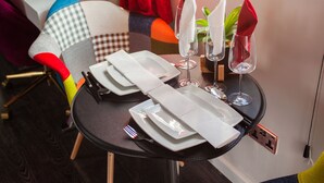 Une table à manger élégamment dressée, avec des assiettes, des couverts et des verres, une chaise aux couleurs vives et une petite plante.