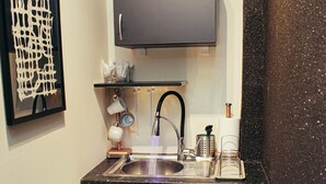 Une cuisine compacte dotée d’un plan de travail noir, d’un évier encastré, d’un four à micro-ondes et d’une petite poubelle.