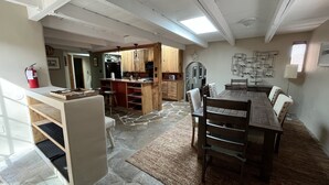 Une cuisine spacieuse dotée de meubles en bois, d’un sol en pierre et d’un coin repas avec une grande table et des chaises.