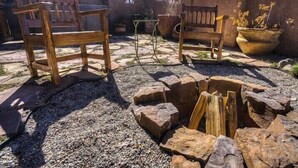 Une terrasse extérieure avec deux bancs en bois, une petite table et un foyer entouré de pierres.