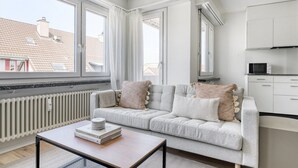 A modern apartment with a grey sofa, a small table with books, and a kitchen area. - Dreamy Iselin 2 Room w/ Storage, 1min to Local Market, by Blueground (Basel)
