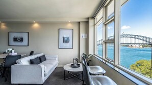 A modern room with a sofa, a small table, and a view of a bridge and harbor. - KozyGuru | McMahons Point | Opera House View (McMahons Point)