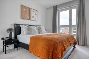 Une chambre moderne avec un grand lit, une table de chevet, une lampe et deux œuvres d’art abstraites encadrées accrochées au mur.