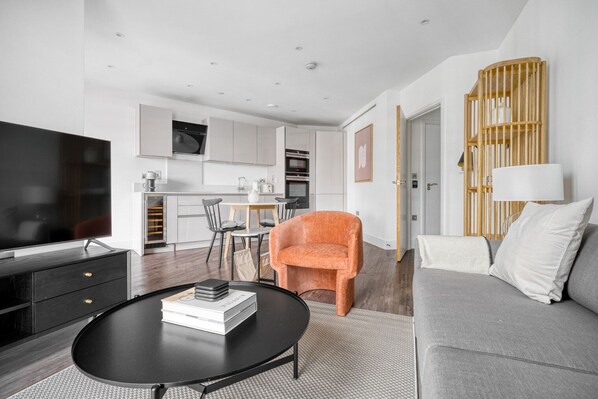 Un salon moderne avec un téléviseur, un canapé et un fauteuil orange.