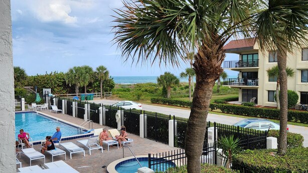 A pool area with lounge chairs, a small pool, and a view of the ocean. - Oceanfront Condo w/ ocean view private balcony, on-site heated pool & hot tub (Cape Canaveral)