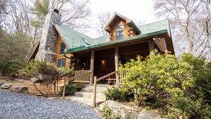 Une cabane en rondins avec une cheminée en pierre, un toit végétalisé et un porche en bois.