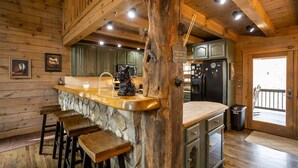 Une cuisine rustique avec un comptoir en pierre, des tabourets en bois et un plafond en bois.