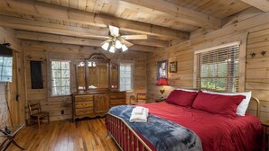 Une chambre dans une cabane en bois, avec un lit, une commode et un ventilateur de plafond.
