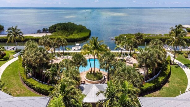 Un resort con piscina centrale, palme e vista sull'oceano.