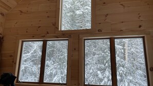 Une cabane dotée de trois fenêtres, chacune offrant une vue sur des arbres couverts de neige.