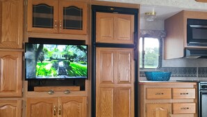 Een keuken met houten kastjes, een ingebouwde televisie en een eettafel.