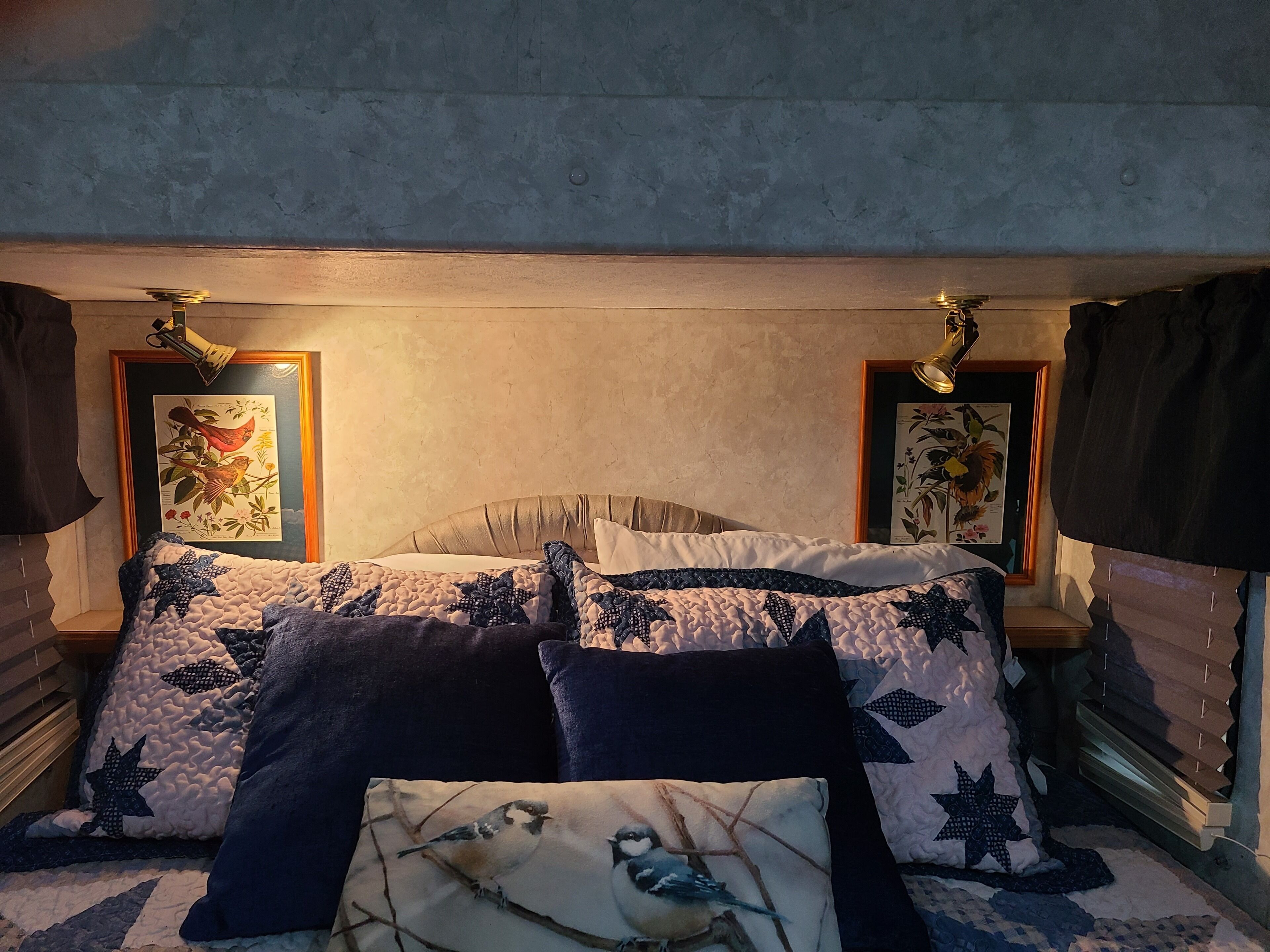 Ein Schlafzimmer mit einem Bett, zwei gerahmten Pflanzenbildern und einem Fenster mit Jalousien.