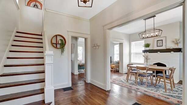 Un hall d’entrée spacieux avec un escalier en bois, un coin repas agrémenté d’un tapis à motifs et une cheminée.