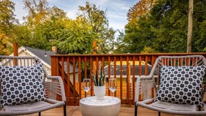 Une terrasse avec deux fauteuils en osier et une petite table, entourée d’une clôture en bois et d’arbres.