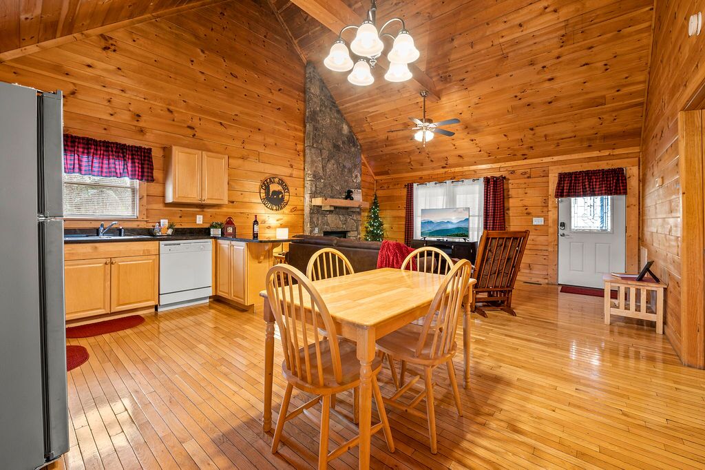 Un acogedor interior de cabaña con paredes de madera, una zona de comedor con mesa y sillas de madera, una cocina con armarios de madera y una chimenea.