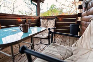 An outdoor seating area with a round table and cushioned chairs, a wooden deck, and string lights. - 1BR Cozy Cabin - Romantic, Hot Tub, Couples, RELAX in Pigeon Forge (Pigeon Forge)