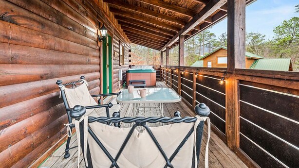 A wooden cabin with a covered porch, a hot tub, and a table with chairs. - 1BR Cozy Cabin - Romantic, Hot Tub, Couples, RELAX in Pigeon Forge (Pigeon Forge)