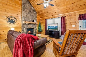 Cozy cabin interior with a stone fireplace, leather sofa, and wooden dining table.
