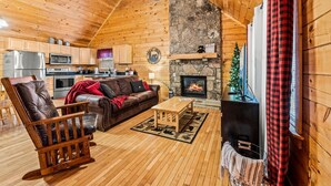 A cozy log cabin interior with a fireplace, wooden furniture, and a stone accent wall. - 1BR Cozy Cabin - Romantic, Hot Tub, Couples, RELAX in Pigeon Forge (Pigeon Forge)