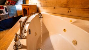 A bathroom with a bathtub, a wooden wall, and a bed with a quilt in the background. - 1BR Cozy Cabin - Romantic, Hot Tub, Couples, RELAX in Pigeon Forge (Pigeon Forge)