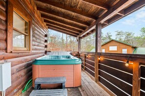 A wooden cabin with a hot tub on a deck, a window, and a view of the surrounding forest. - 1BR Cozy Cabin - Romantic, Hot Tub, Couples, RELAX in Pigeon Forge (Pigeon Forge)