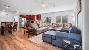 A spacious living room with a large sectional sofa, a dining area with wooden chairs, and a kitchen with red cabinets.