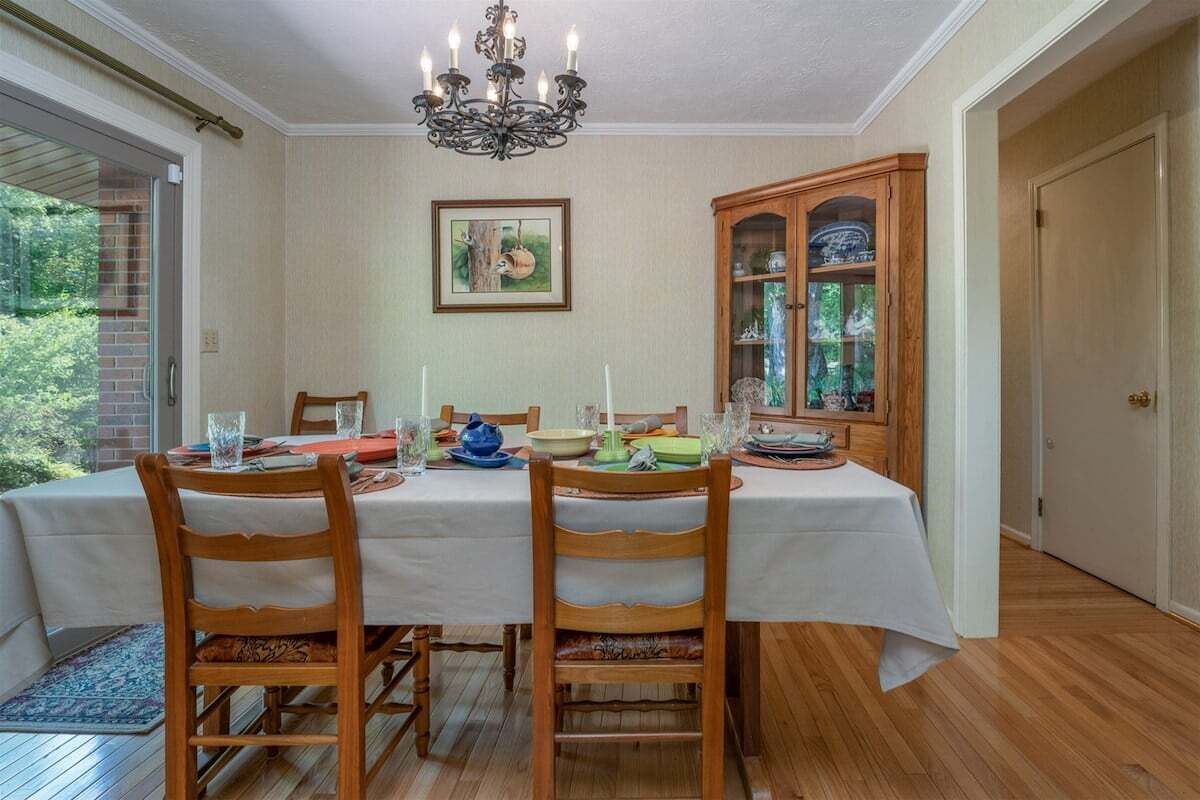 A dining room with a table set for four, wooden chairs, a chandelier, a cabinet with glass doors, and a framed picture on the wall.