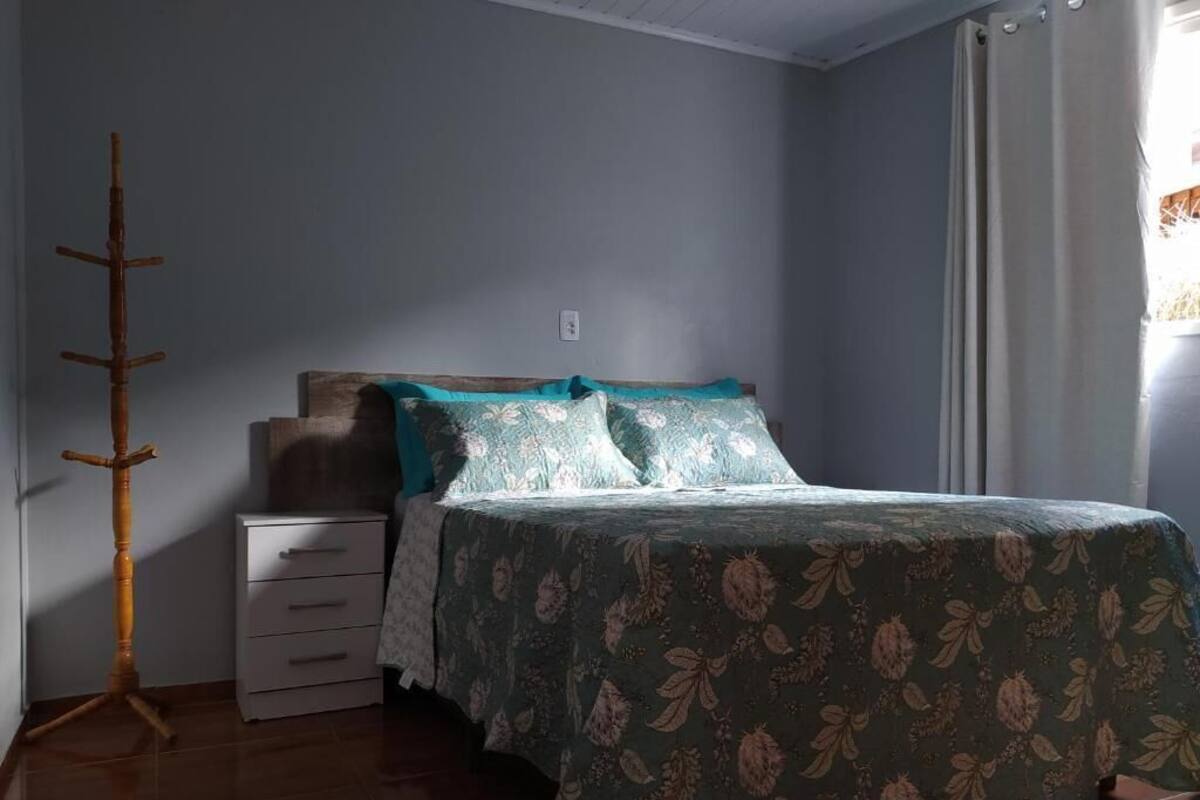 A bedroom with a bed, a nightstand, a wooden coat rack, and a window with curtains.