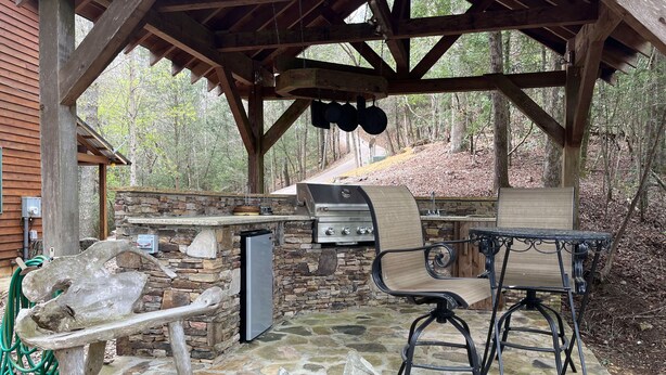 An outdoor patio with a stone floor, a stone wall, a grill, a table with chairs, and a wooden swing. - Paradise Valley private with a Romatic Stream (Dahlonega)