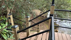 A wooden staircase with black railings leading to a wooden deck over a flowing river. - Paradise Valley private with a Romatic Stream (Dahlonega)