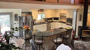 A spacious kitchen with a central island, stainless steel appliances, and a stone fireplace. - Paradise Valley private with a Romatic Stream (Dahlonega)