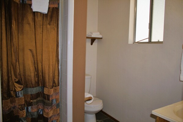 Un baño con inodoro, lavamanos, ventana y cortina de ducha.