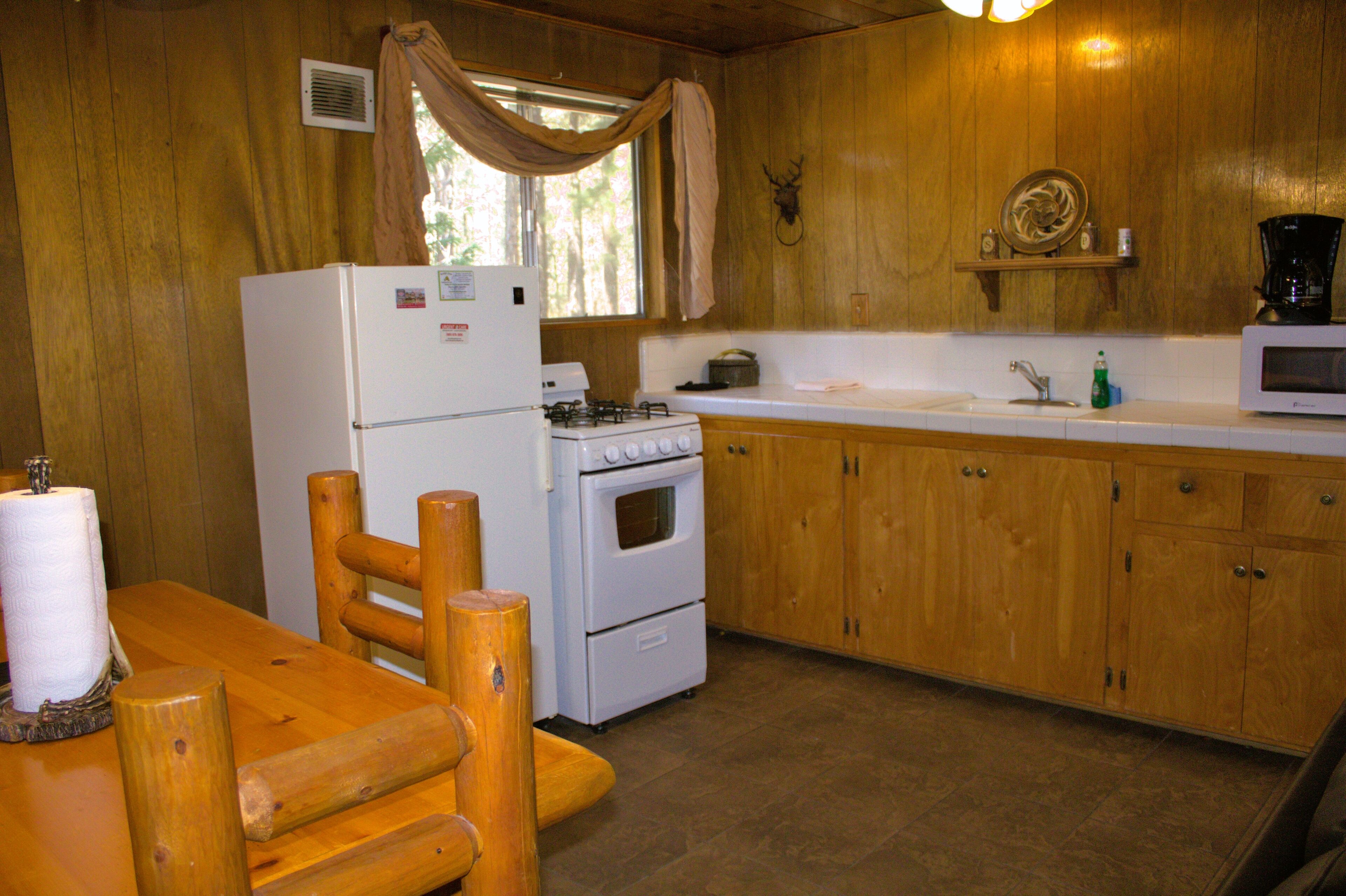 A wooden cabin kitchen with a refrigerator, stove, microwave, and wooden cabinets.