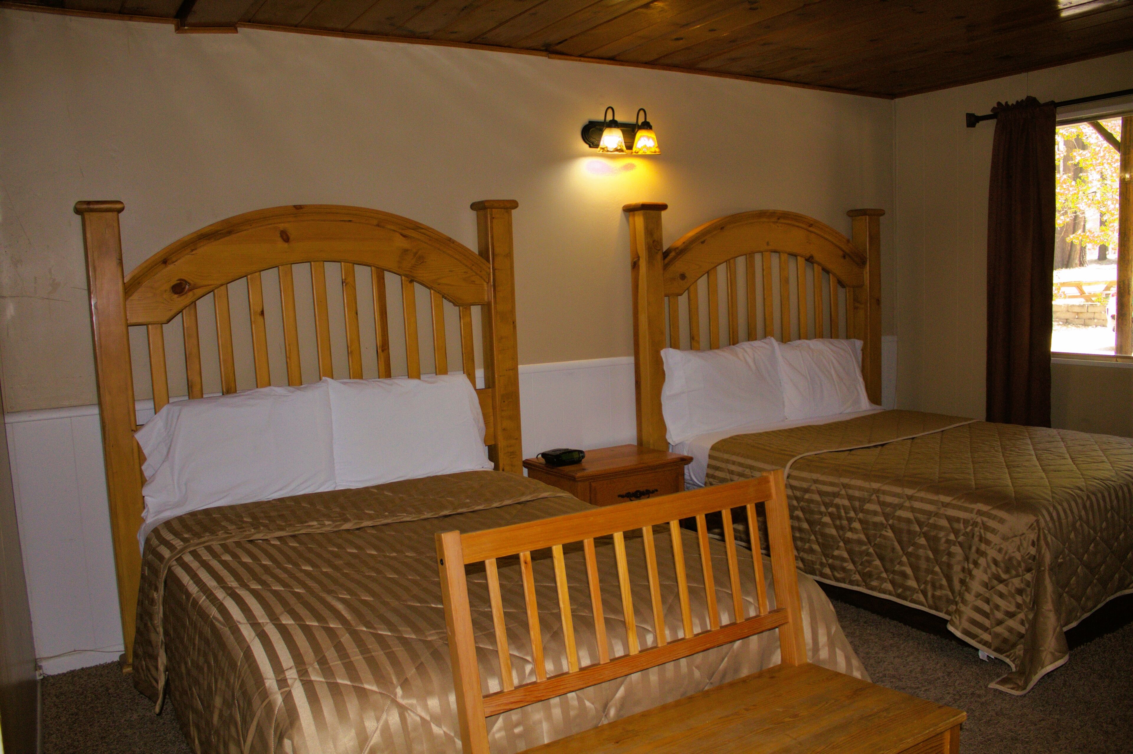 Quarto com duas camas de madeira, cada uma com cabeceira, mesa de cabeceira e luminária fixada na parede.