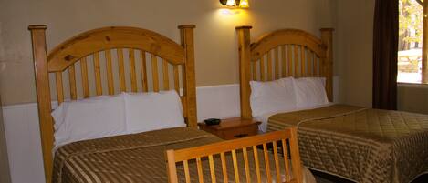 Quarto com duas camas de madeira, cada uma com cabeceira, mesa de cabeceira e luminária fixada na parede.