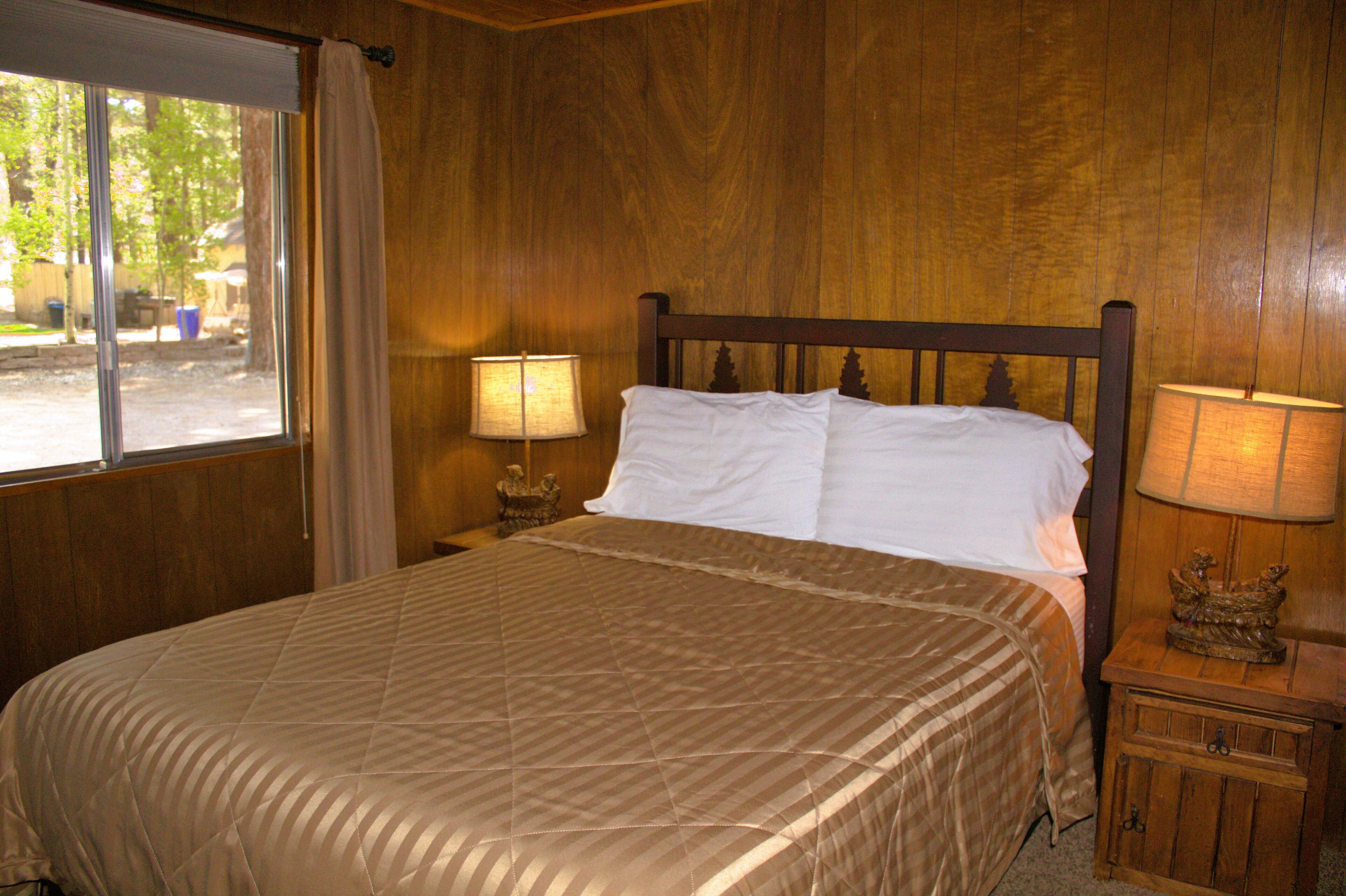 A neatly made bed with a brown quilt, two bedside lamps, and a small wooden nightstand with a decorative item.